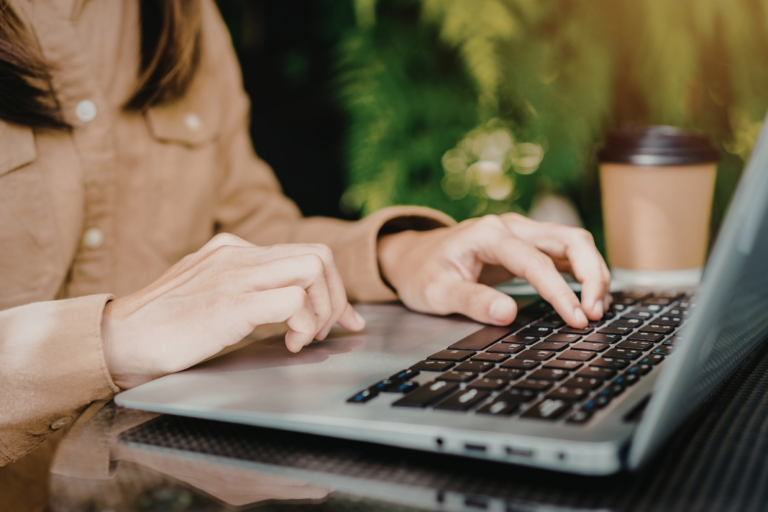woman working on laptop. Greenery in the background, coffee nearby. Web builder. Digital Agency